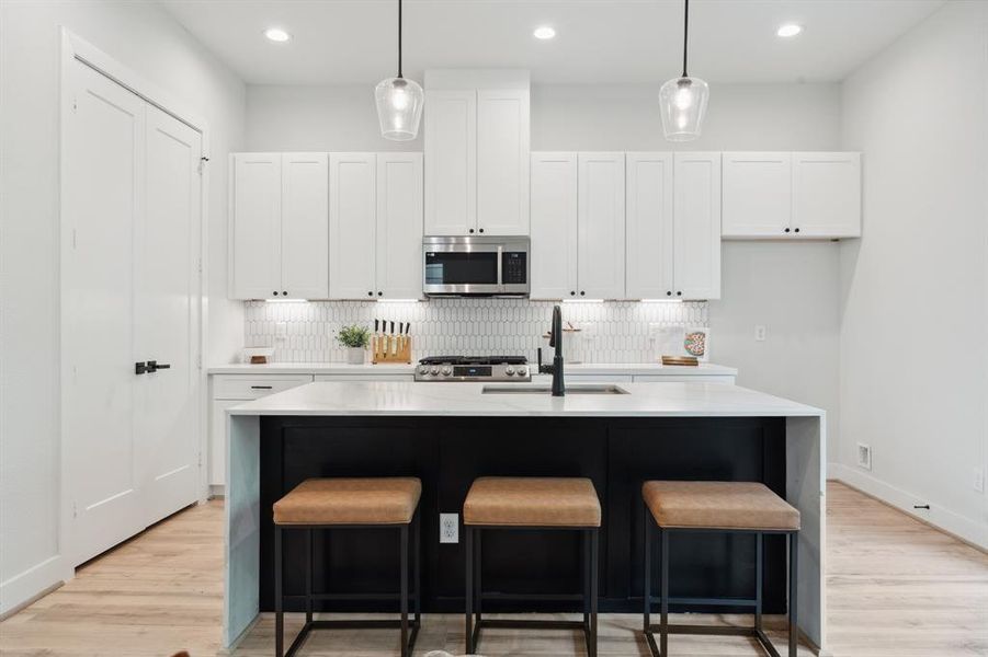 The kitchen, accented by a three-seater waterfall island, blends soft-close cabinets and polished black finishes harmoniously with elegant pendant lighting.