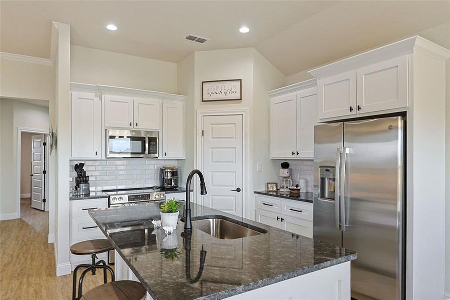 Kitchen featuring a large island with sink, white shaker cabinetry, stainless steel appliances, and a subway tile backsplash