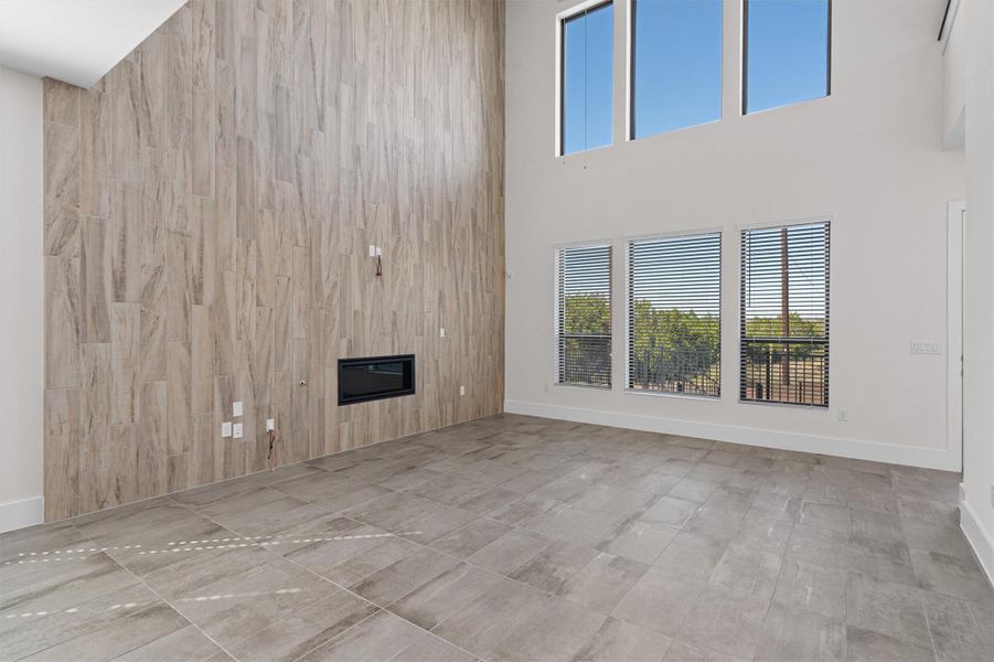 Unfurnished living room featuring a high ceiling, wood walls, and a glass covered fireplace Unfurnished living room featuring a high ceiling, wood walls, and a glass covered fireplace