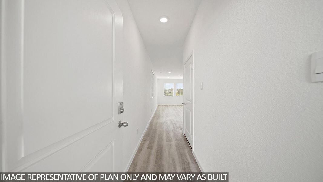 Interior hallway featuring light wood-finish flooring, white walls, recessed ceiling lighting, and a white interior door with a silver handle