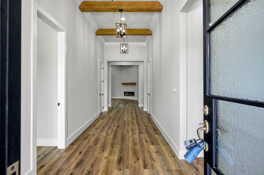 The grand entry showcases 12’ ceilings, wood beams and wood and iron pendant lighting. Warm wood tone LVP is featured throughout the home. The grand entry showcases 12’ ceilings, wood beams and wood and iron pendant lighting. Warm wood tone LVP is featured throughout the home.