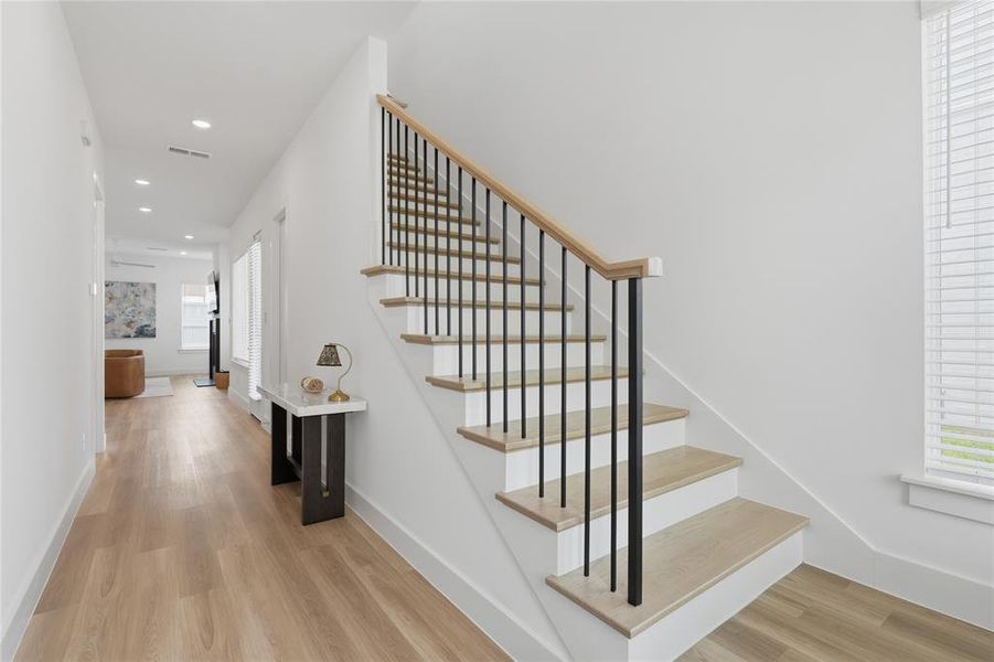 Staircase featuring wood-finish treads, white risers, and a contemporary black metal baluster system with a natural wood handrail