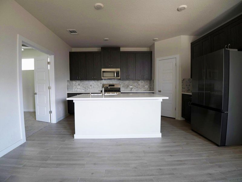 Kitchen with appliances with stainless steel finishes, decorative backsplash, an island with sink, and light wood-type flooring Kitchen with appliances with stainless steel finishes, decorative backsplash, an island with sink, and light wood-type flooring