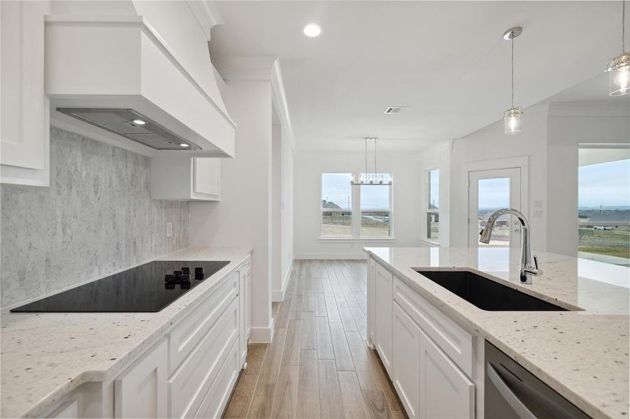 Kitchen with sink, pendant lighting, white cabinets, and custom exhaust hood