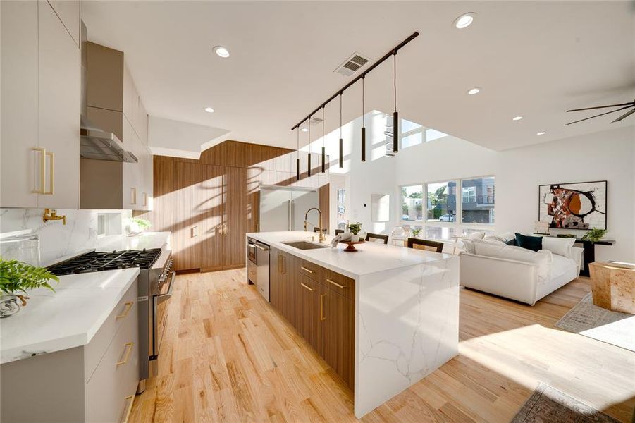 Kitchen with light hardwood / wood-style floors, a kitchen island with sink, sink, and wall chimney range hood