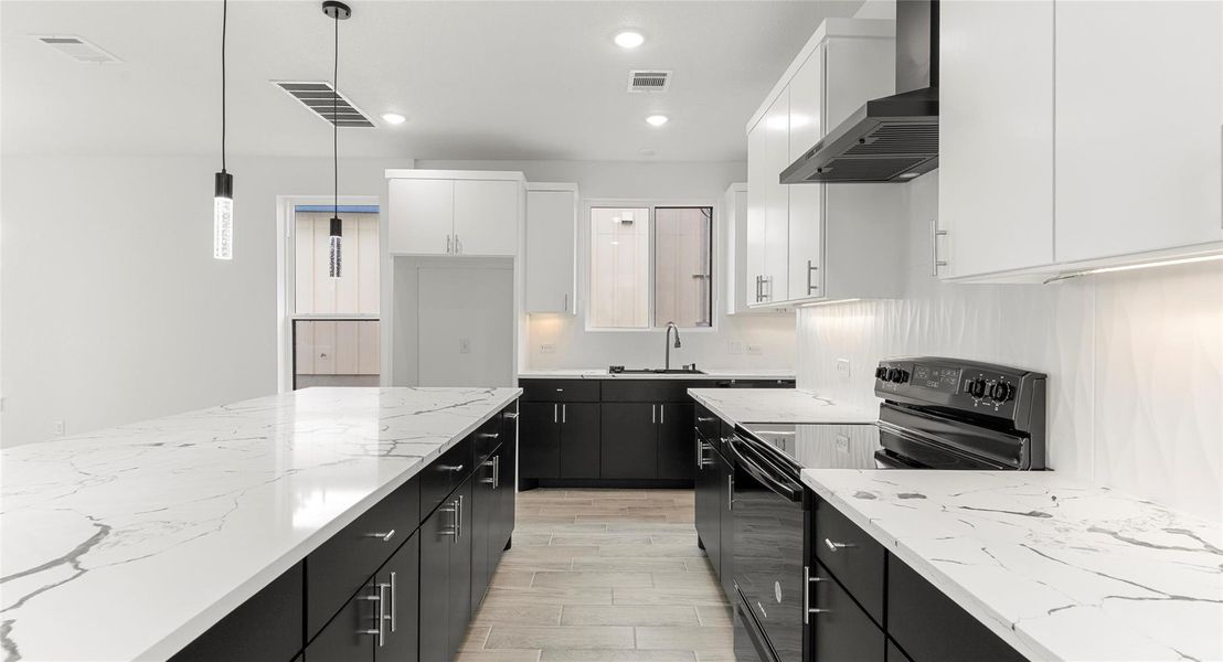 Kitchen with dark cabinetry, black range with electric stovetop, wall chimney exhaust hood, decorative light fixtures, and light stone countertops