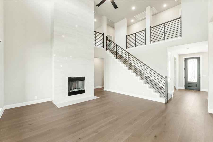 Open living room with two-story ceiling, white tile fireplace, hardwood floors, and staircase with black metal railing Open living room with two-story ceiling, white tile fireplace, hardwood floors, and staircase with black metal railing