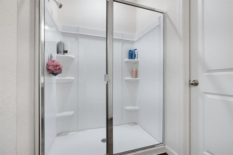 Walk-in shower with a glass enclosure and chrome hardware, featuring a showerhead and multiple built-in shelving units
