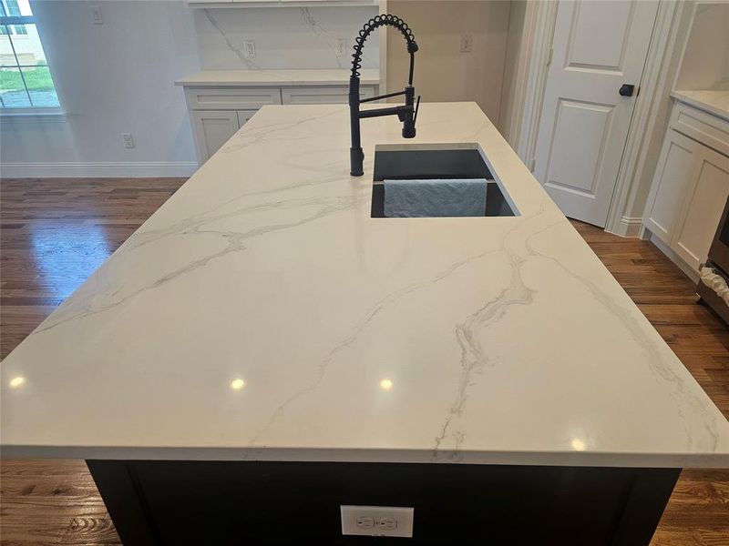 white cabinetry, a center island with sink, dark hardwood / wood-style floors, and light stone countertops