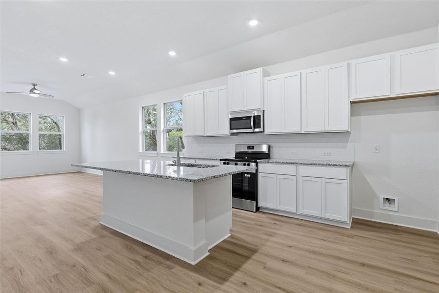 Kitchen with stainless steel appliances, white cabinetry, light stone countertops, a center island with sink, and recessed lighting