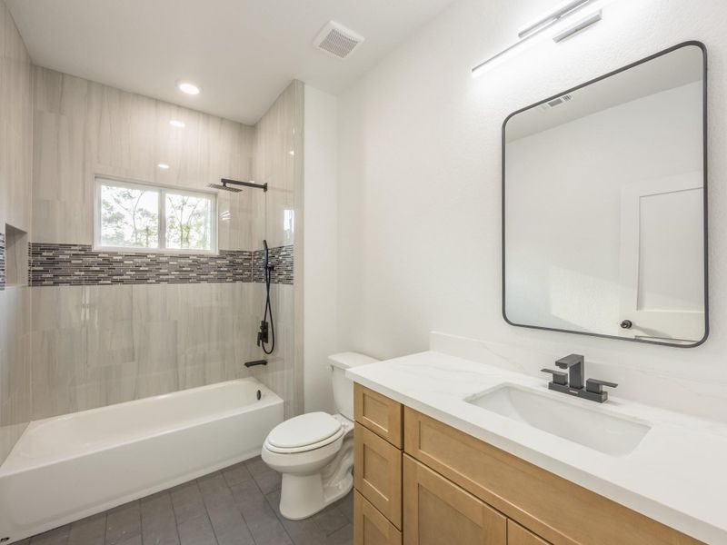 The guest bath features a combination tub/shower with stunning vertical tile surround and mosaic accent, quartz countertop, and modern matte black hardware. The guest bath features a combination tub/shower with stunning vertical tile surround and mosaic accent, quartz countertop, and modern matte black hardware.