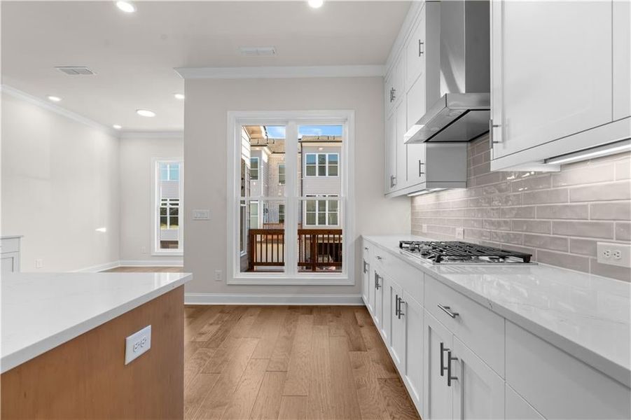 Kitchen featuring light stone counters, crown molding, backsplash, light wood-type flooring, and white cabinets