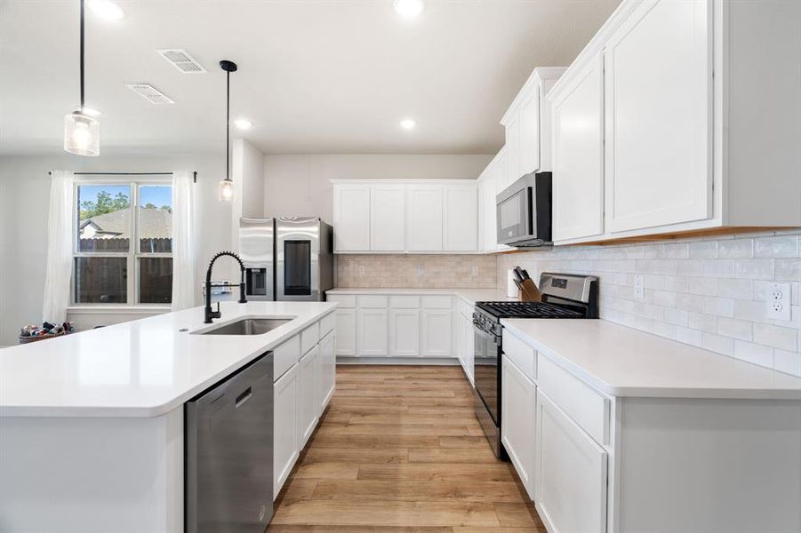 Kitchen featuring appliances with stainless steel finishes, pendant lighting, white cabinetry, decorative backsplash, and a kitchen island with sink Kitchen featuring appliances with stainless steel finishes, pendant lighting, white cabinetry, decorative backsplash, and a kitchen island with sink