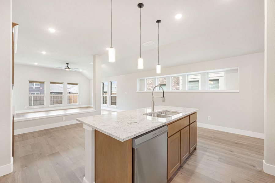 Kitchen island with granite countertop, sink, and pendant lights, open to living area with hardwood floors