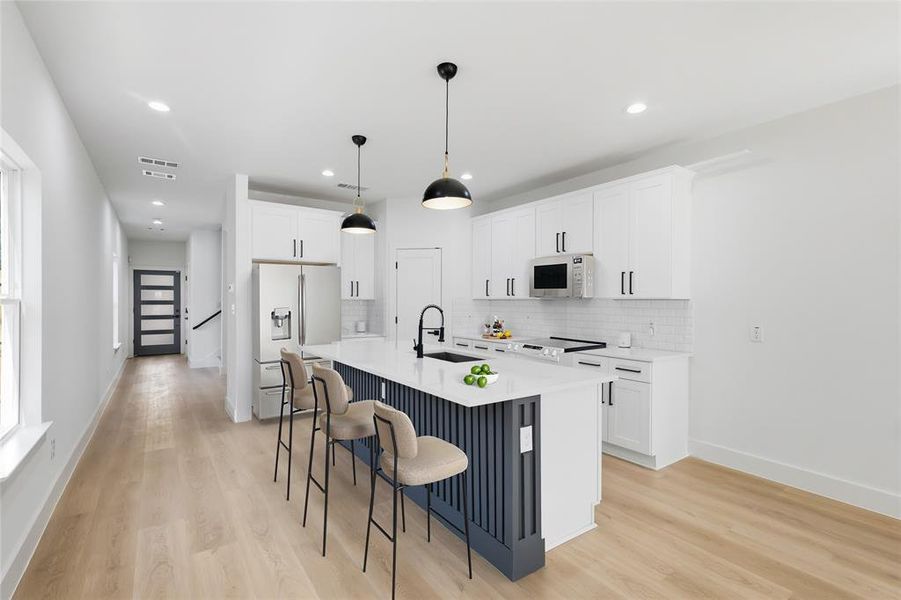 Kitchen featuring decorative backsplash, white cabinetry, fridge with ice dispenser, light wood finished floors, and recessed lighting Kitchen featuring decorative backsplash, white cabinetry, fridge with ice dispenser, light wood finished floors, and recessed lighting