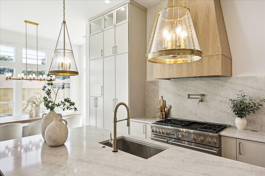 Designed for both function and wow factor, the kitchen pairs a Thermador range with a custom white oak vent hood, Taj Mahal natural quartzite countertops, Visual Comfort lighting, and a deep prep sink with Delta fixtures that keeps the family chef right in the middle of the action.