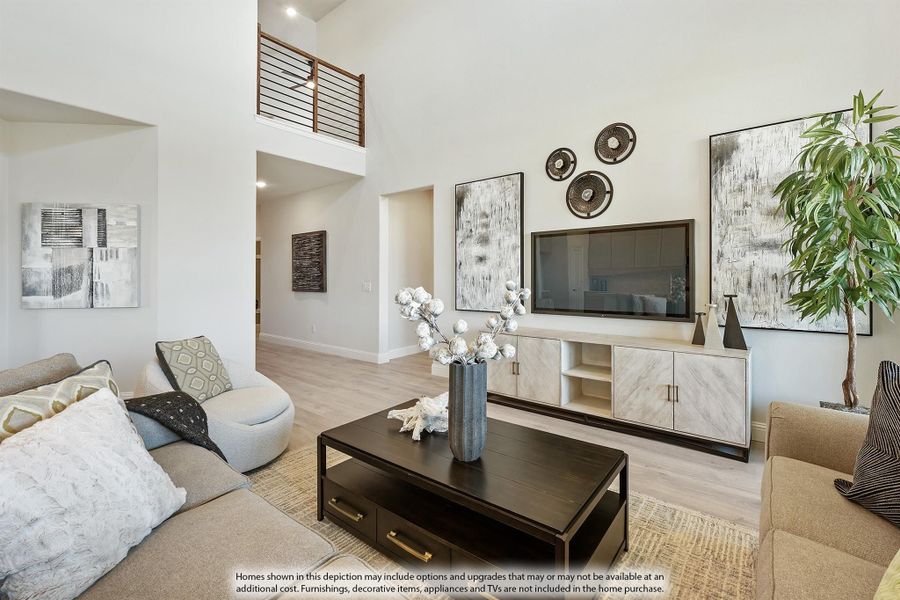 Living room with two-story ceiling, wall-mounted TV, light wood floors, and second-floor balcony overlook.