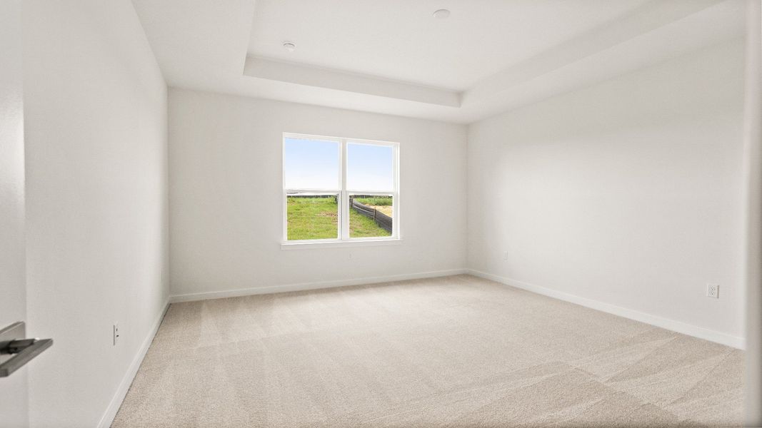 Spacious primary bedroom with tray ceiling, plush carpet, and abundant natural light in the Castaway model