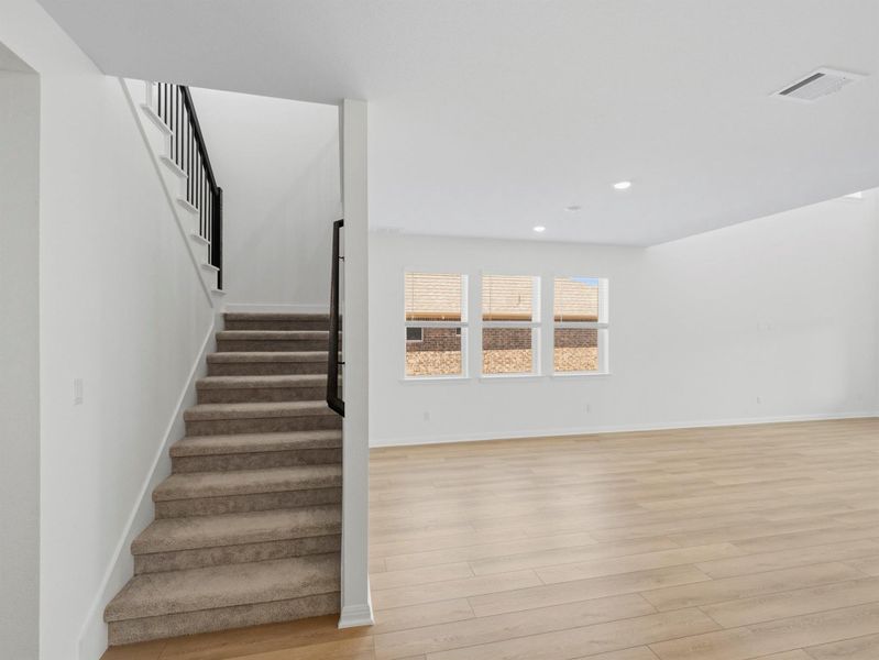 A graceful staircase ascends alongside a naturally illuminated living area featuring sleek wood flooring. A graceful staircase ascends alongside a naturally illuminated living area featuring sleek wood flooring.