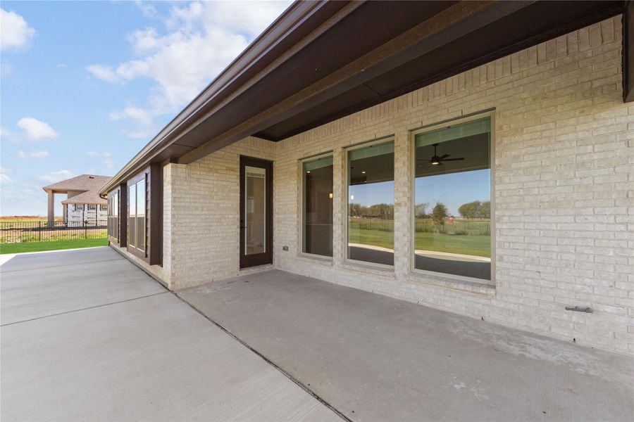 Covered concrete patio along brick home exterior with large windows and dark-framed back door
