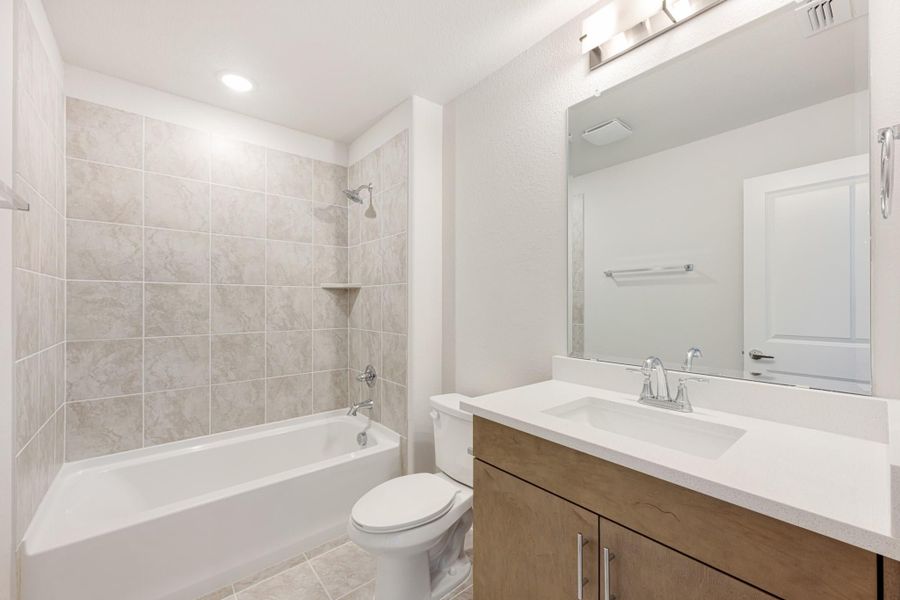 Bathroom with tiled tub and shower, wood vanity with white countertop, and large mirror
