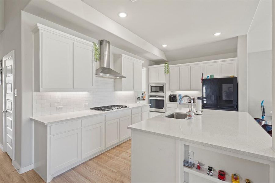Kitchen with white cabinetry, decorative backsplash, light stone counters, recessed lighting, and wall chimney exhaust hood Kitchen with white cabinetry, decorative backsplash, light stone counters, recessed lighting, and wall chimney exhaust hood