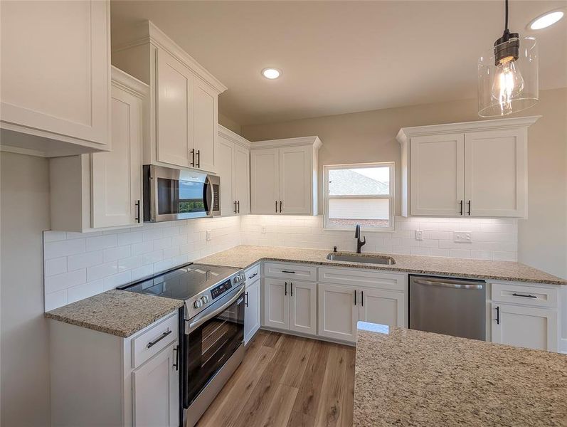 Kitchen with appliances with stainless steel finishes, white cabinetry, light wood finished floors, light stone countertops, and recessed lighting Kitchen with appliances with stainless steel finishes, white cabinetry, light wood finished floors, light stone countertops, and recessed lighting