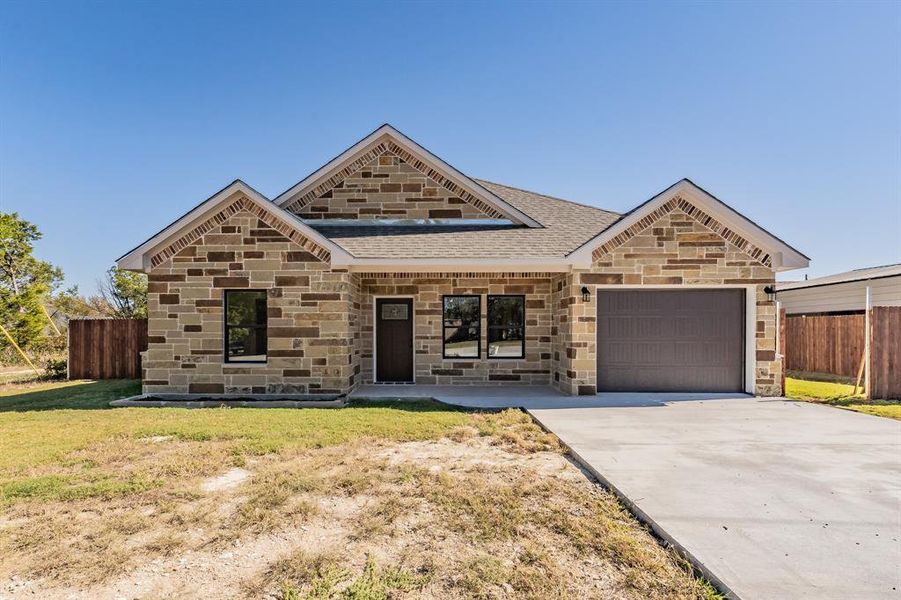View of front facade featuring covered porch, stone siding, an attached garage, driveway, and roof with shingles