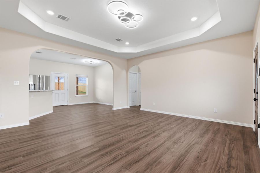 Unfurnished living room with arched walkways, dark wood-style flooring, recessed lighting, and a raised ceiling