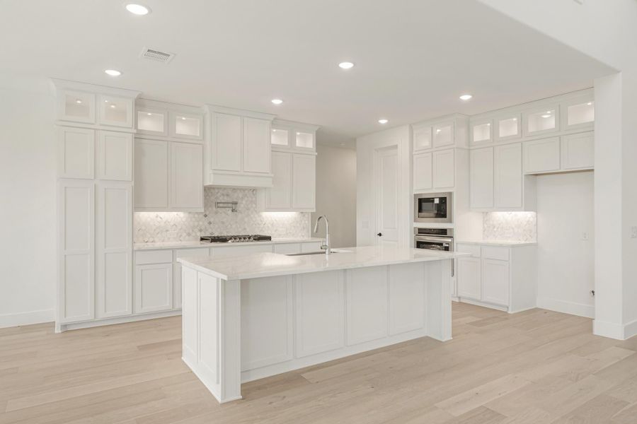 White kitchen with tall cabinets, large center island, marble backsplash, and light hardwood floors
