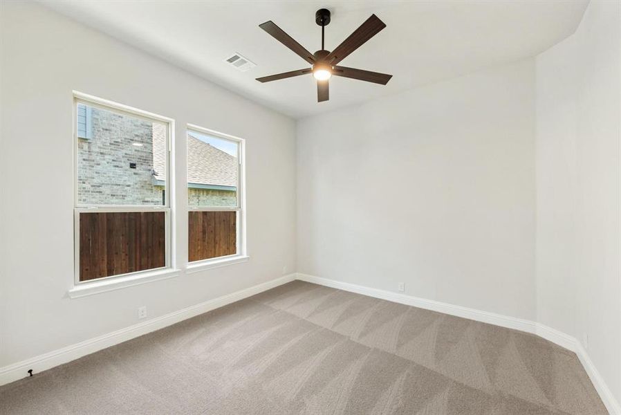 Neutral-toned room featuring a dark wood-finish ceiling fan with integrated lighting, two double-hung windows, and light gray patterned carpet Neutral-toned room featuring a dark wood-finish ceiling fan with integrated lighting, two double-hung windows, and light gray patterned carpet