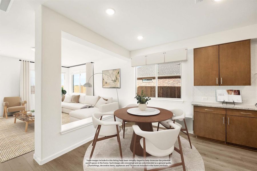 Open dining area with round wood table and white chairs, adjacent to living room and kitchen with brown cabinets