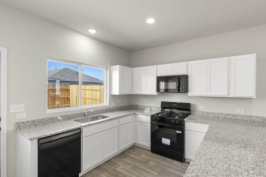 Image of a U-shaped kitchen with white cabinets, black appliances, a window above the sink, and white trim Image of a U-shaped kitchen with white cabinets, black appliances, a window above the sink, and white trim