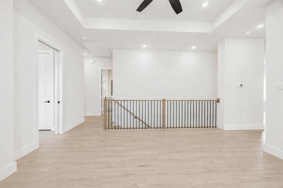 Spacious open concept room featuring light wood-finish flooring, white walls, and a tray ceiling with recessed lighting