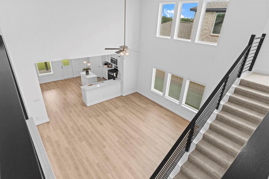 A dramatic bird’s-eye view of the two-story living area reveals the expansive woodlike tile flooring, soaring ceilings, and walls of windows that flood the space with natural light. **Image Representative of Plan Only and May Vary as Built**.