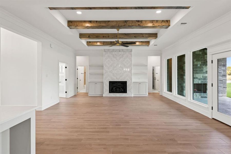Unfurnished living room featuring a high end fireplace, beamed ceiling, light wood finished floors, and ceiling fan Unfurnished living room featuring a high end fireplace, beamed ceiling, light wood finished floors, and ceiling fan