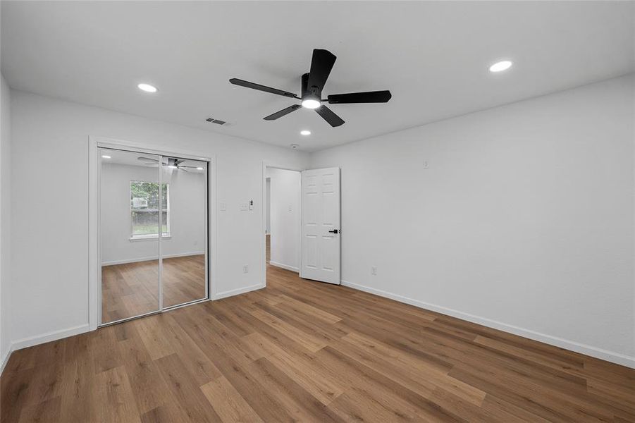 Spacious room featuring wood-finish flooring, a contemporary ceiling fan, recessed lighting, and mirrored closet doors Spacious room featuring wood-finish flooring, a contemporary ceiling fan, recessed lighting, and mirrored closet doors