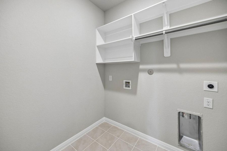 Functional laundry room featuring built-in shelving and tile flooring for effortless utility.