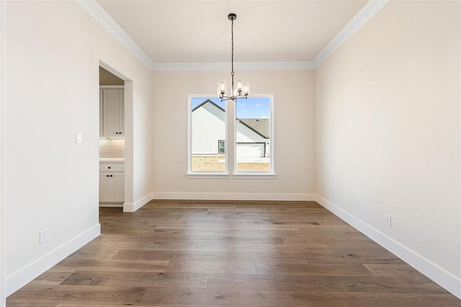 Unfurnished dining area with a chandelier, crown molding, and dark wood-style floors