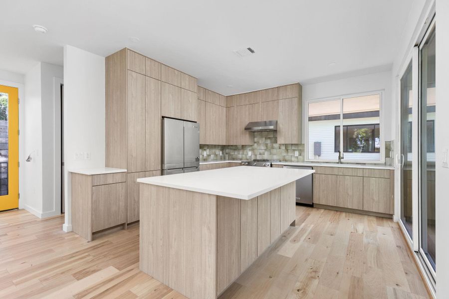 Kitchen with stainless steel appliances, light brown cabinetry, modern cabinets, and light wood-type flooring
