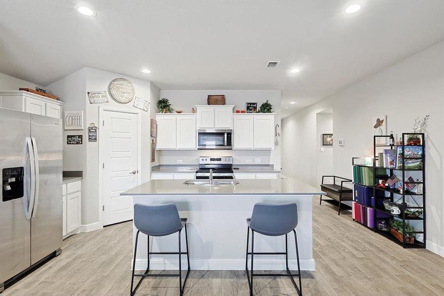 Kitchen with stainless steel appliances, light countertops, white cabinets, and visible vents