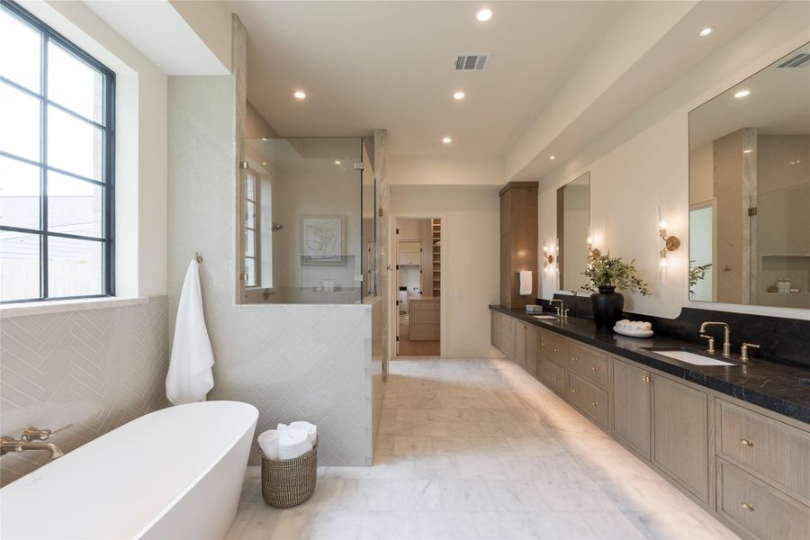 The primary bath blends tranquility and high design, offering a spa-inspired atmosphere layered with soft textures and organic tones. A sculptural Victoria & Albert freestanding tub is framed by a wall of glossy herringbone tile, adjacent to an expansive glass-enclosed shower trimmed in stone. The full-length custom vanity is topped with dark honed countertops and features brass plumbing fixtures and double mirrors softly lit by sconces. The primary bath blends tranquility and high design, offering a spa-inspired atmosphere layered with soft textures and organic tones. A sculptural Victoria & Albert freestanding tub is framed by a wall of glossy herringbone tile, adjacent to an expansive glass-enclosed shower trimmed in stone. The full-length custom vanity is topped with dark honed countertops and features brass plumbing fixtures and double mirrors softly lit by sconces.