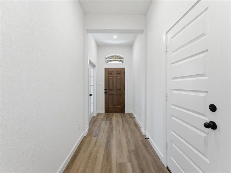 Inviting entryway featuring wood-finish flooring, a solid wood entry door with an arched transom window, and a white paneled interior door with matte black hardware Inviting entryway featuring wood-finish flooring, a solid wood entry door with an arched transom window, and a white paneled interior door with matte black hardware