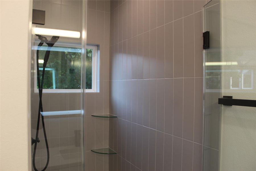 Modern shower with sleek glass enclosure and corner shelving.