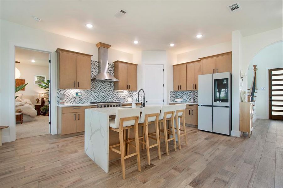 Kitchen featuring a breakfast bar, smart refrigerator, a center island with sink, light stone countertops, and tasteful backsplash Kitchen featuring a breakfast bar, smart refrigerator, a center island with sink, light stone countertops, and tasteful backsplash