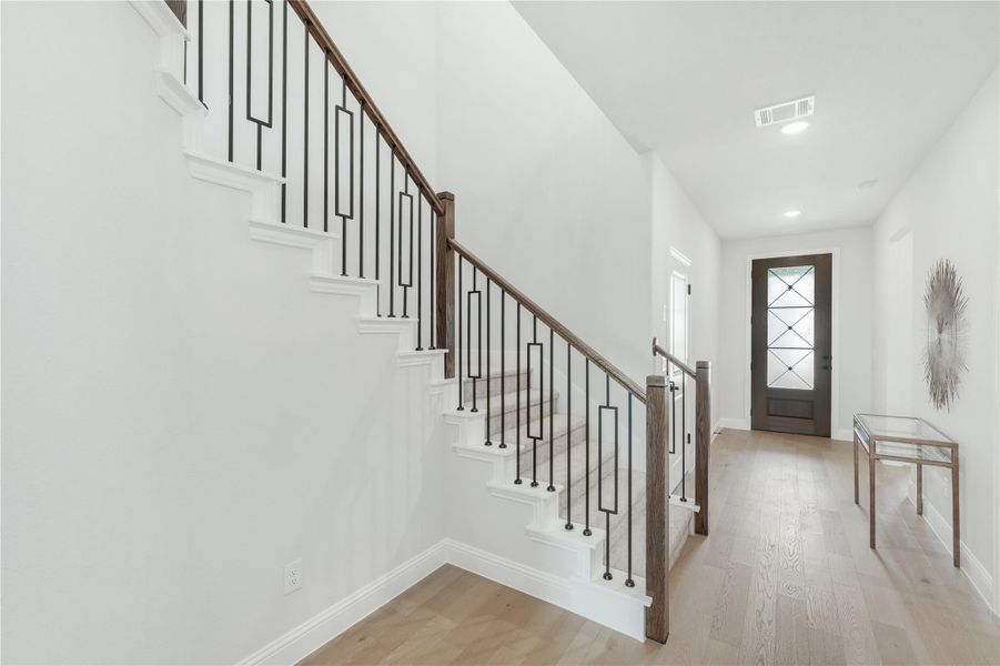Bright entryway with staircase featuring iron balusters, wood handrail, and light hardwood floors leading to front door
