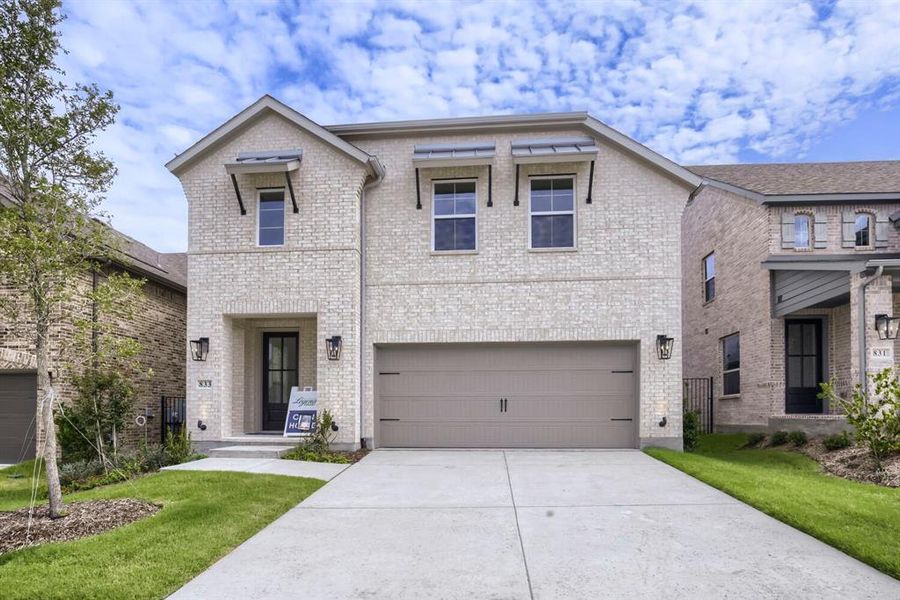 Two-story brick facade residence featuring a two-car garage, covered entry, and decorative window awnings