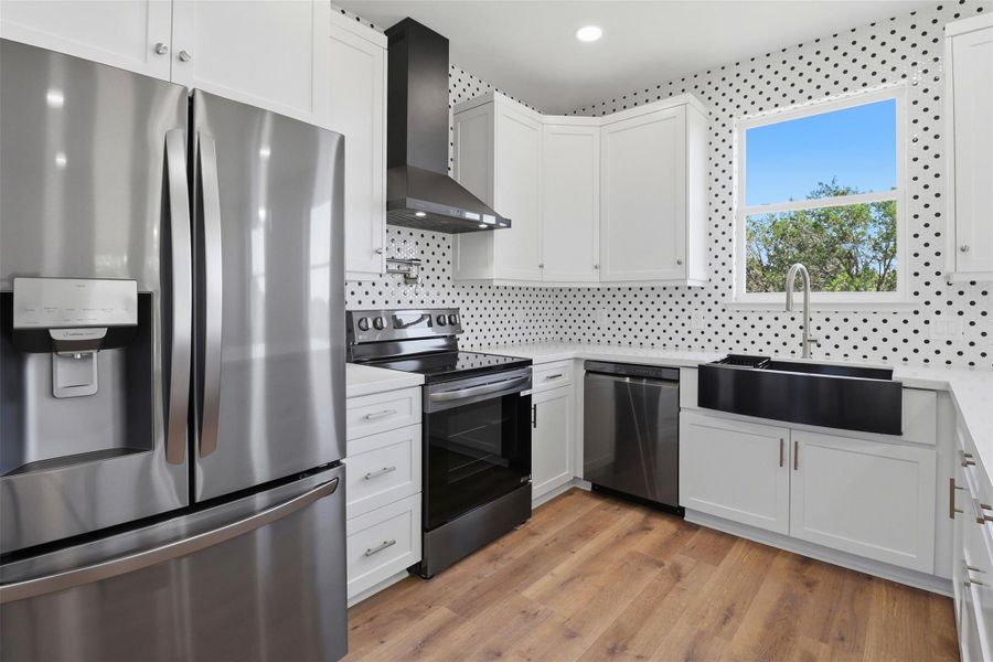 Kitchen featuring white cabinetry, stainless steel appliances, a black farmhouse sink, and wood-finish flooring Kitchen featuring white cabinetry, stainless steel appliances, a black farmhouse sink, and wood-finish flooring