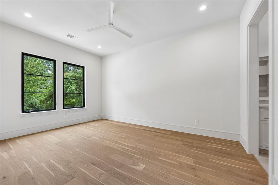 Black framed windows fill this secondary bedroom with natural light, while wide plank hardwoods and an ensuite bath create a comfortable, private retreat for family or guests.
