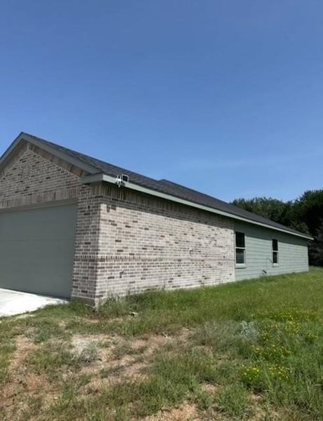 View of side of home featuring brick siding, an attached garage, concrete driveway, and a lawn View of side of home featuring brick siding, an attached garage, concrete driveway, and a lawn